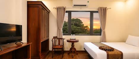 Quarto de hotel com televisão, armário de madeira, pequena mesa com garrafas de água, cama e janela com cortinas.