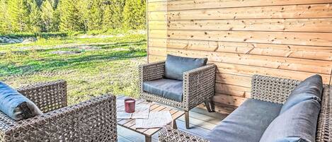 Una terraza de madera con mobiliario de mimbre y vistas a una ladera boscosa.