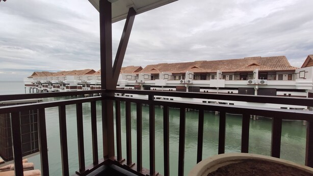 A view of overwater bungalows with a wooden balcony railing, connected by walkways to the water.