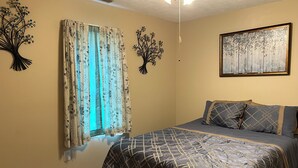 Ein Schlafzimmer mit Bett, blumigen Vorhängen, Wandbildern und einer Deckenleuchte.