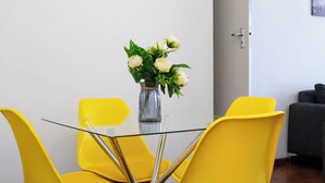 A dining table with a glass top surrounded by four yellow chairs, a vase with white flowers, and a gray couch in the background. - Apartment Sleeps 4, 2 Baths, Free Parking (Harare)