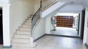 A staircase with a metal railing leading to a landing. There is a large open space with a tiled floor and a view of a brick building through an open doorway. - Apartment Sleeps 4, 2 Baths, Free Parking (Harare)