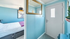 Un dormitorio con cama, mesita de noche, lámpara, espejo y puerta.