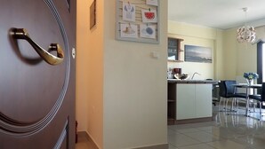Una cocina moderna con una isla central, un comedor con sillas y un pasillo que lleva a una puerta con manija de latón.