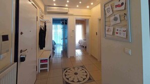 Un pasillo de hotel con suelo de baldosas, un radiador, un perchero, una mesita y una pared adornada con cuadros.