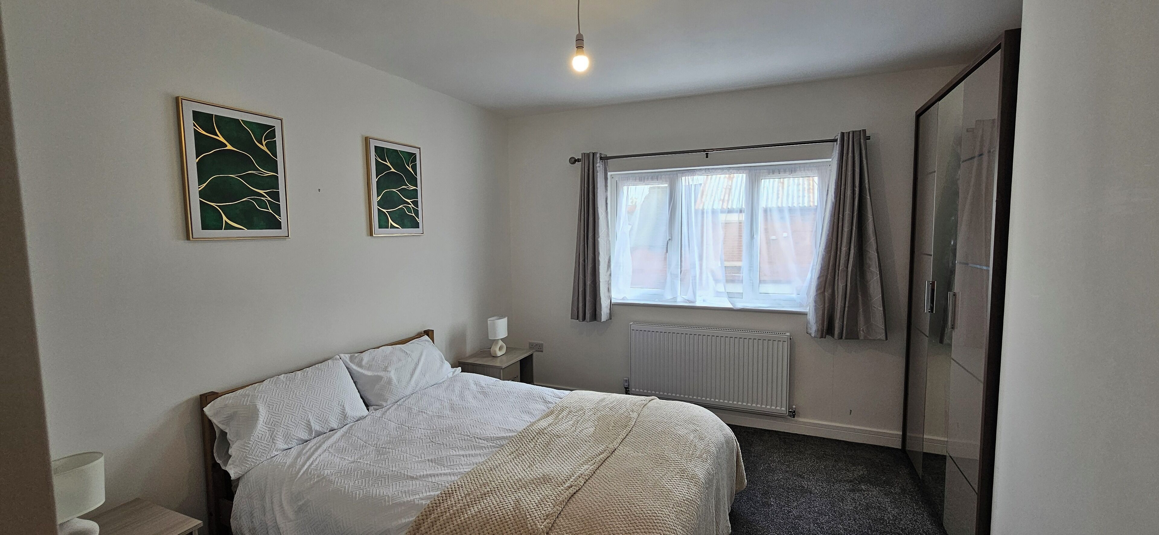 A bedroom with a bed, a nightstand, a radiator, and two framed artworks on the wall.