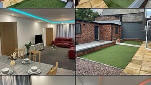 Une maison moderne avec une façade en briques, une pelouse bien entretenue et un coin repas où une table est dressée pour quatre personnes.