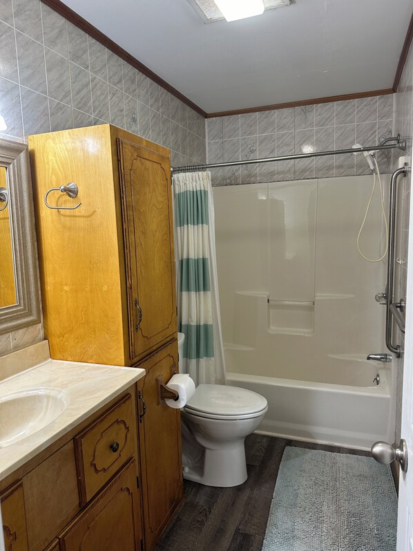 Un bany amb un lavabo de fusta, un vàter, una dutxa amb porta de vidre i un penjador de tovalloles.
