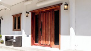 A white building with a large wooden door and two windows. There are wicker chairs and a small table outside. - Cozy Studio Apartment.  Pet Friendly! (Sayulita)
