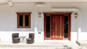 A white building with a wooden door and two windows, a small table with chairs, and two wall-mounted lanterns. - Cozy Studio Apartment.  Pet Friendly! (Sayulita)