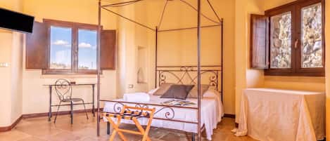 A four-poster bed with a wooden frame, a small table with a white tablecloth, and a chair with a metal frame.