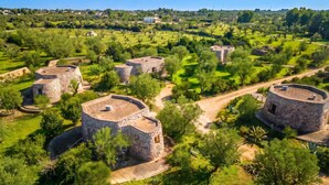 Une série de constructions en pierre, dotées de toits plats, entourées d’une végétation luxuriante et surplombées par un ciel dégagé.
