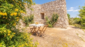 A stone building with a table and chairs in front, surrounded by greenery and flowers. - Pagliara Il Morige 6 In The Countryside, Galatone, Italy (Galatone)