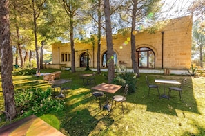 An outdoor patio area with tables and chairs, surrounded by trees and a stone building with arched windows. - Pagliara Il Morige 2 In The Countryside, Galatone, Italy (Galatone)