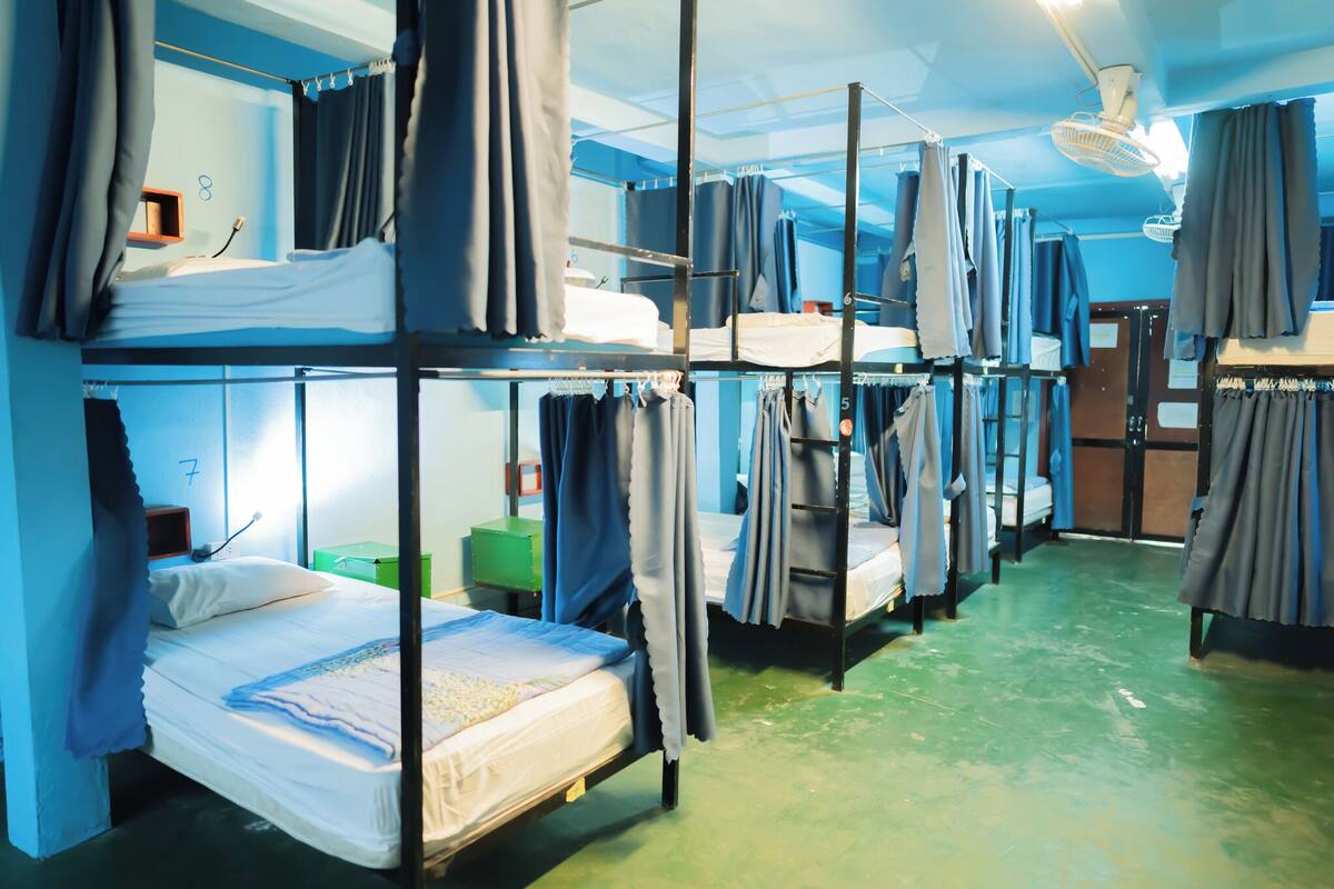 Une chambre de dortoir avec des lits superposés, une poubelle verte et un ventilateur au plafond.