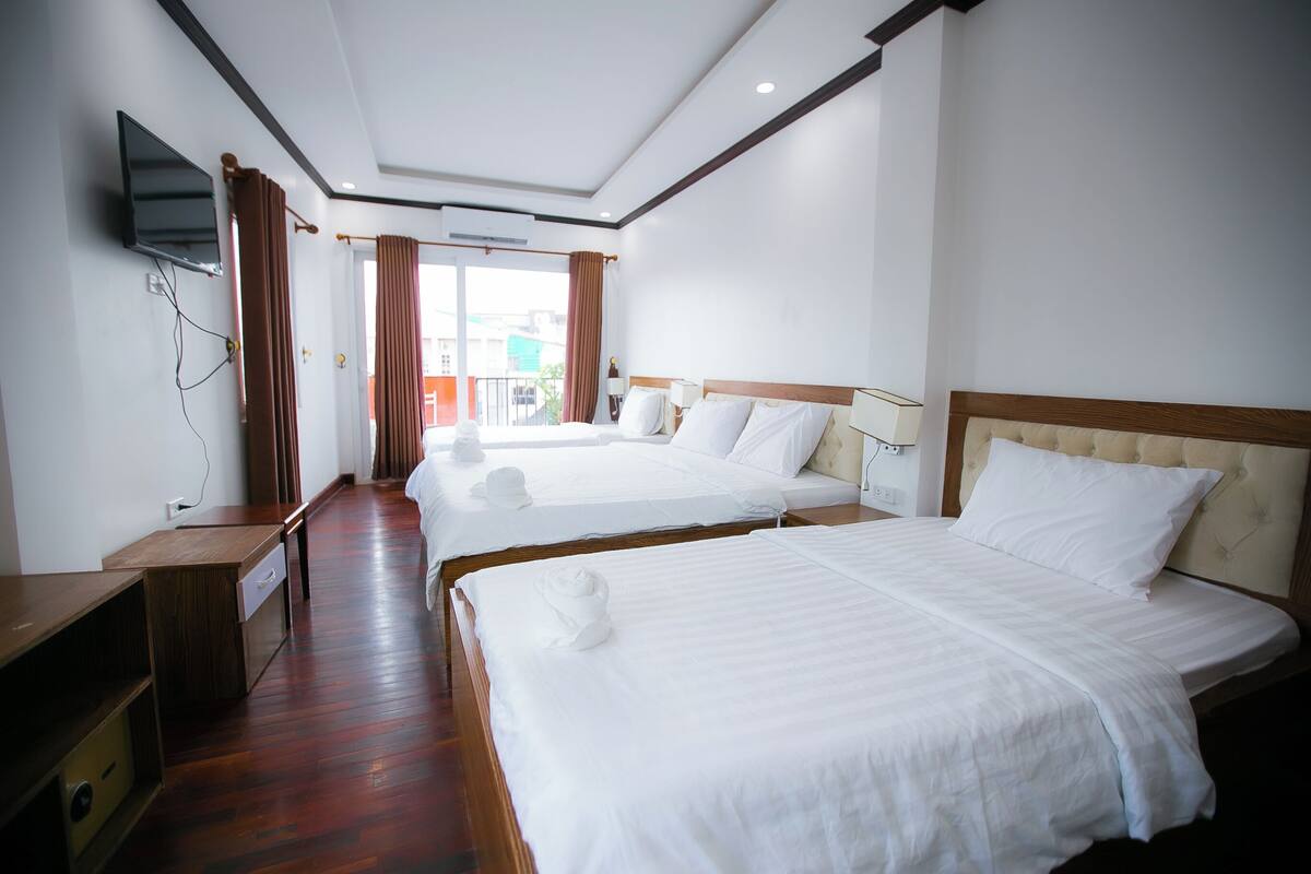 Une chambre d’hôtel avec deux lits, un téléviseur fixé au mur, un bureau en bois et une vue sur l’extérieur.