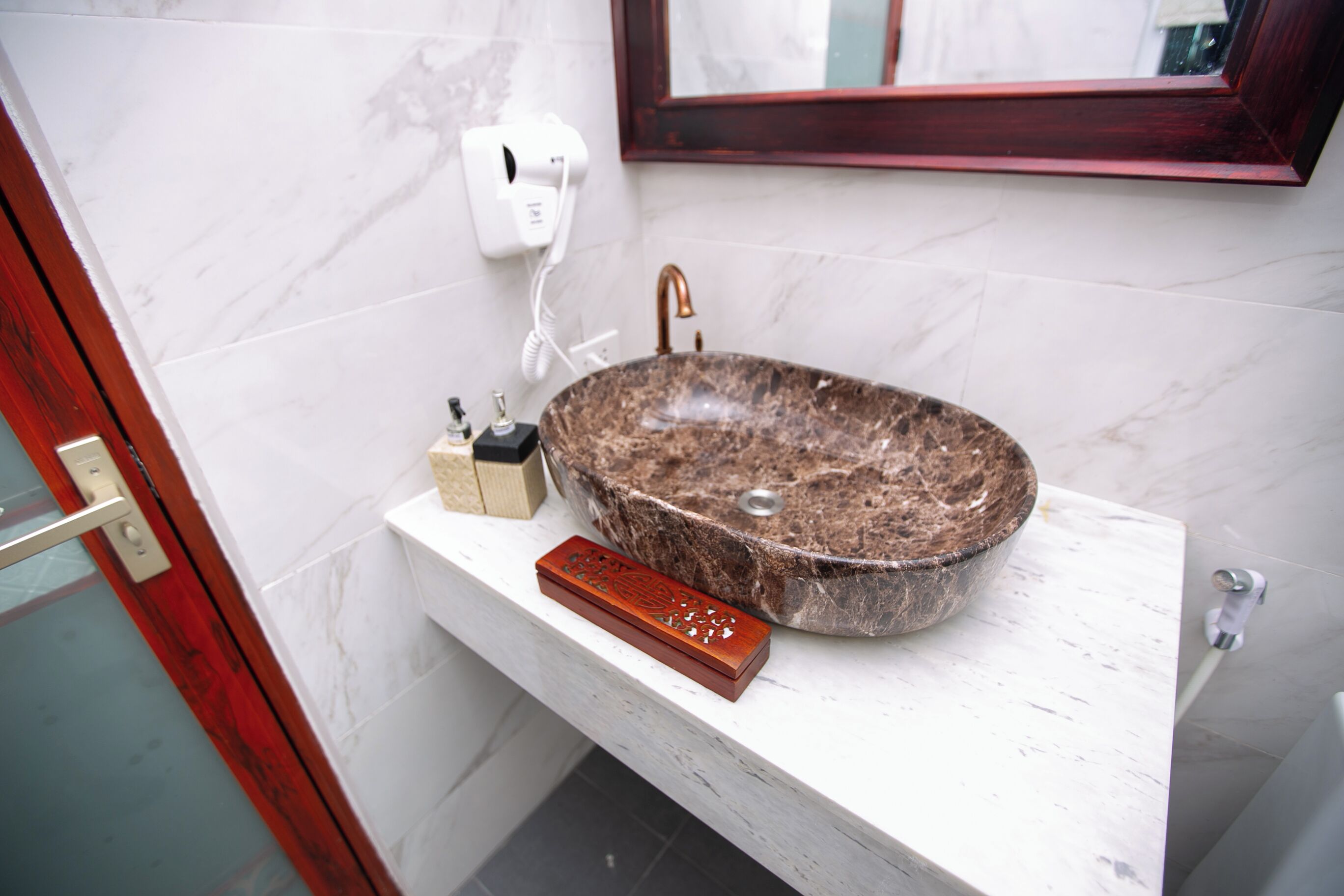 A bathroom with a marble sink, a hairdryer, and a wooden tray.