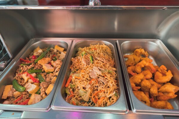 Un buffet proposant trois plats différents : de la viande sautée aux légumes, des nouilles aux légumes et des crevettes frites.