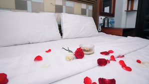Una cama bien hecha con sábanas blancas, un candelabro de vidrio y pétalos de rosa esparcidos.