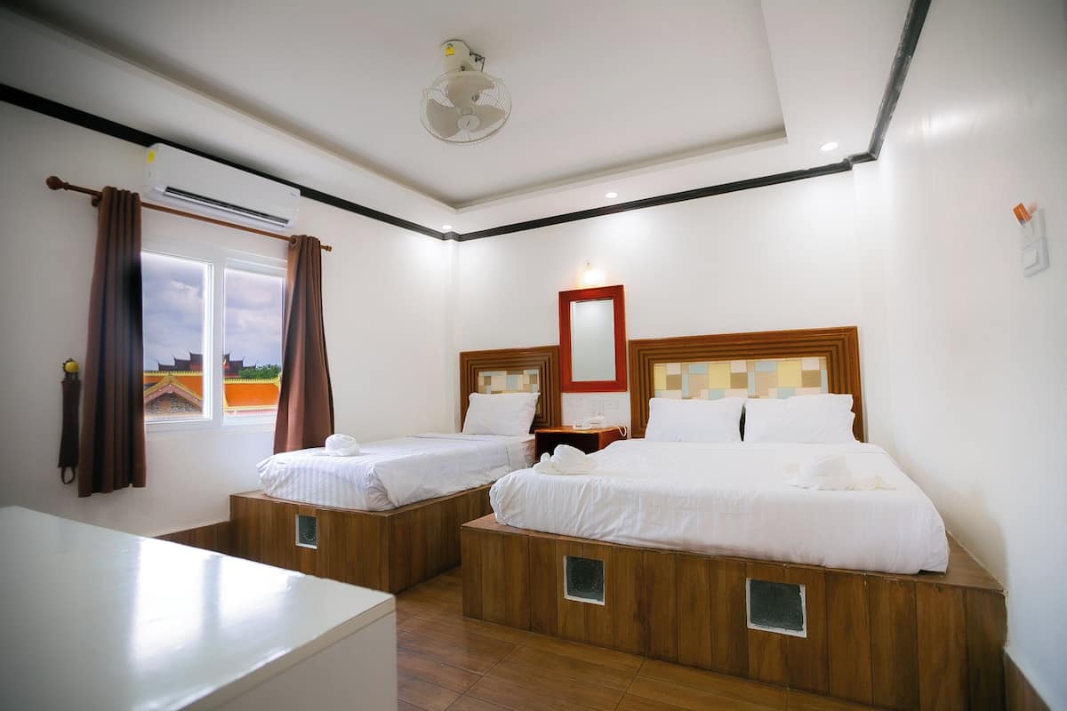 Une chambre d’hôtel avec deux lits, un bureau, un climatiseur, une fenêtre avec des rideaux et un ventilateur de plafond.