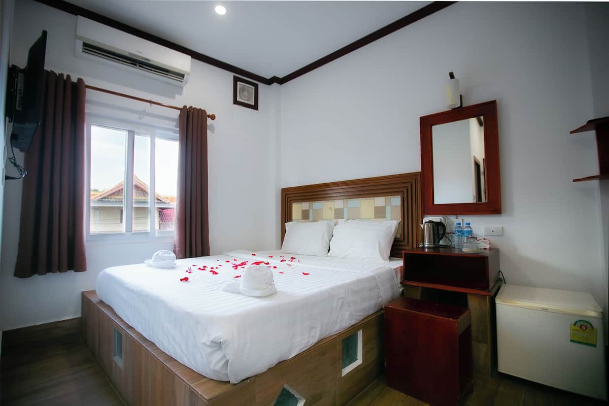 Une chambre d’hôtel avec un lit, un petit bureau, un miroir et un réfrigérateur.