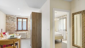 A modern hotel room with a large bed, a bathroom with a mirror, and a dining area with a table and chairs. - Appartamento 30 NODI Torbole 2min walk to Lake, Torbole sul Garda, Italy (Torbole sul Garda)