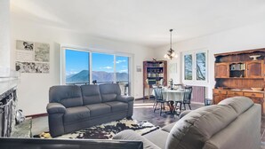 A living room with a sofa, a dining table with chairs, a bookshelf, and a view of mountains through large windows. - Lago Azzurro Villa: Infinity Lake View, Premeno, Italy (Premeno)