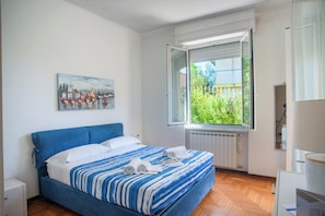 Een slaapkamer met een bed, een raam met uitzicht, een radiator en een schilderij aan de muur.