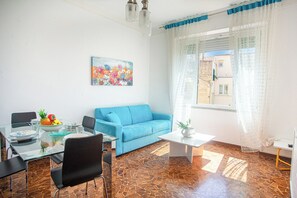 Ein Wohnzimmer mit blauem Sofa, einem Esstisch mit Stühlen, einem Couchtisch und einem Bild an der Wand.