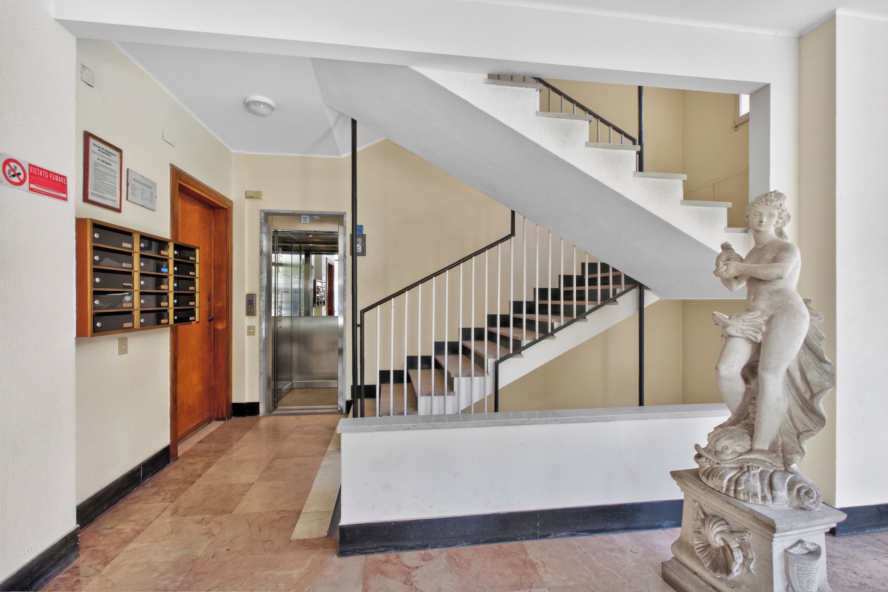 Eine Lobby mit Marmorboden, einer Treppe, einer Statue und einer Reihe von Schließfächern.