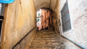A narrow stairway with a metal handrail, leading to a building with a visible window and a door at the top.