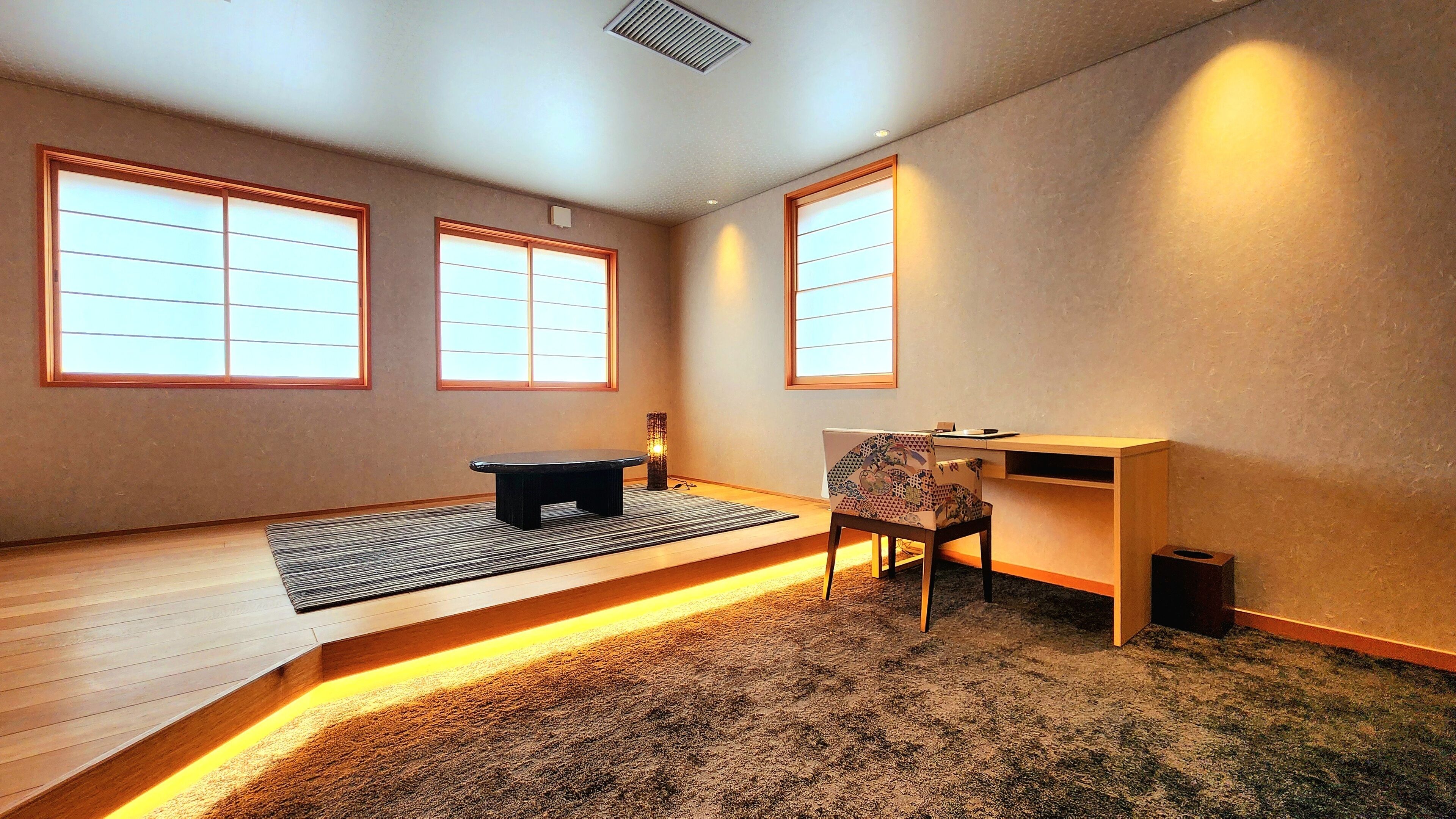 Una habitación con suelo de tatami, un escritorio bajo de madera, una silla y un banco negro.