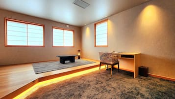 Una habitación con suelo de tatami, un escritorio bajo de madera, una silla y un banco negro.