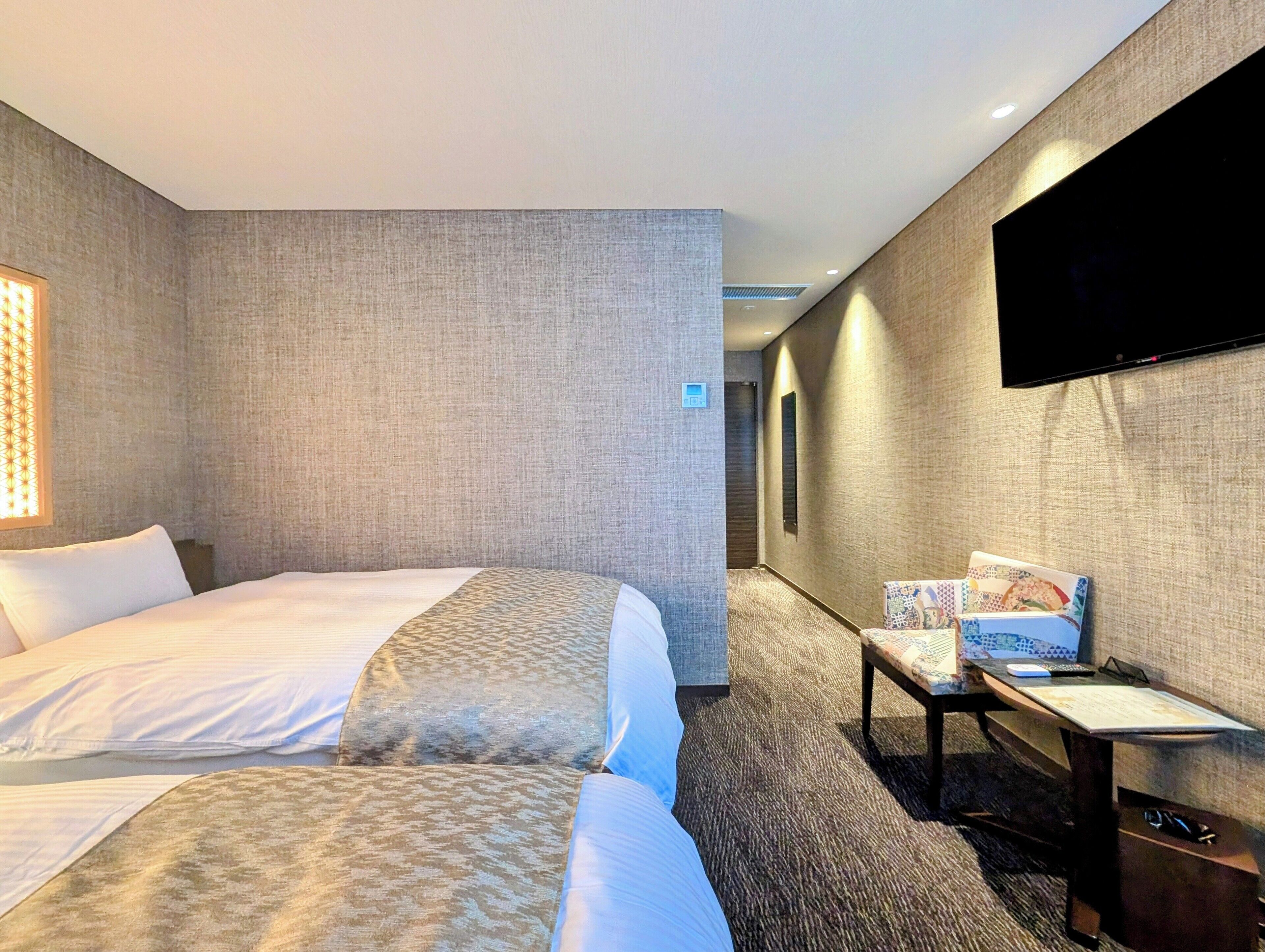 A hotel room with two beds, a TV, a desk, and a carpeted floor.