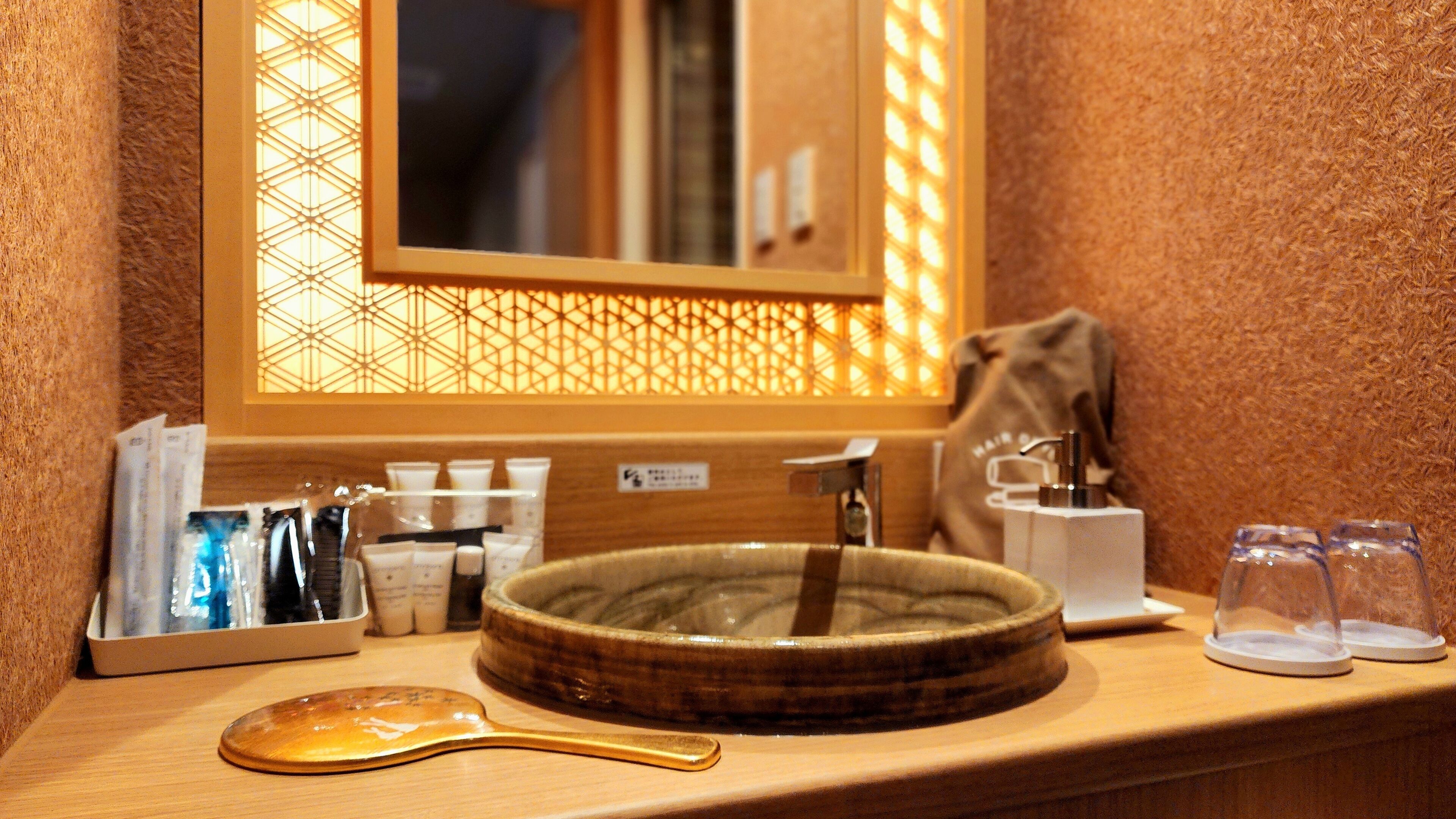 A bathroom with a wooden vanity, a round sink, a mirror, and toiletries.