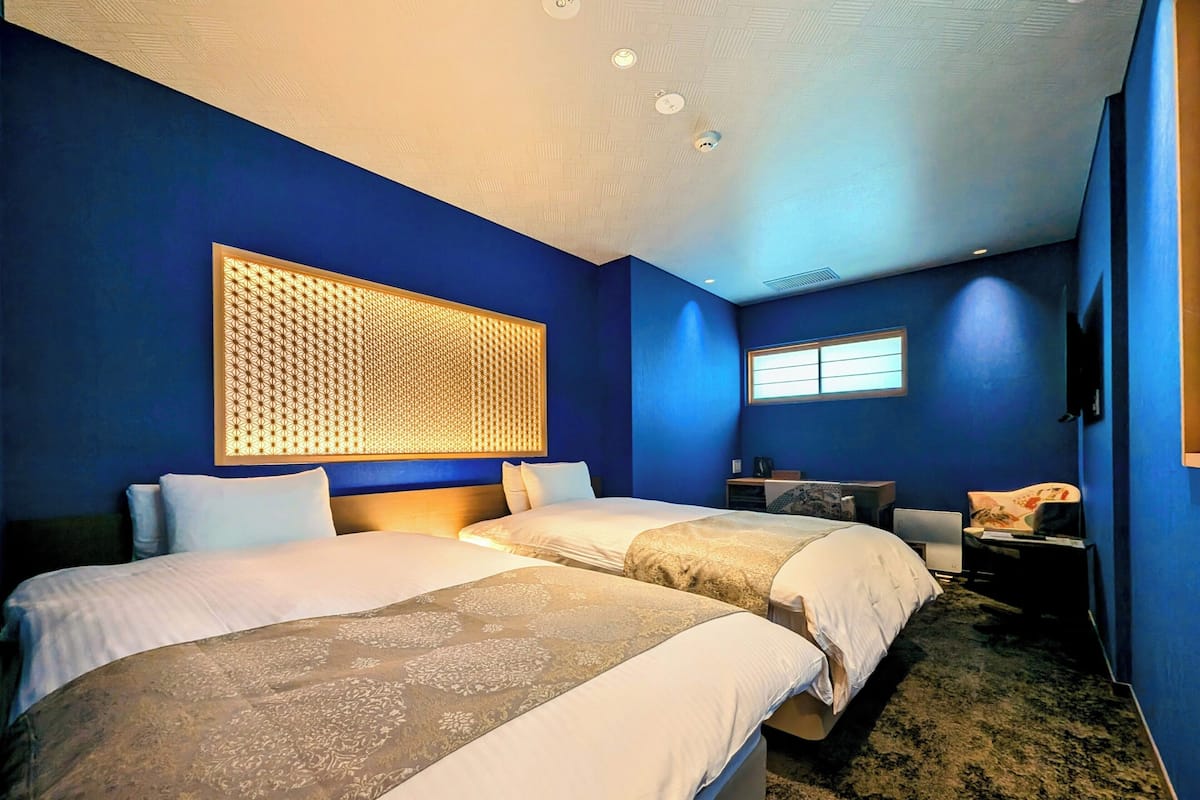 Une chambre d’hôtel avec deux lits, un bureau, une chaise et une fenêtre.