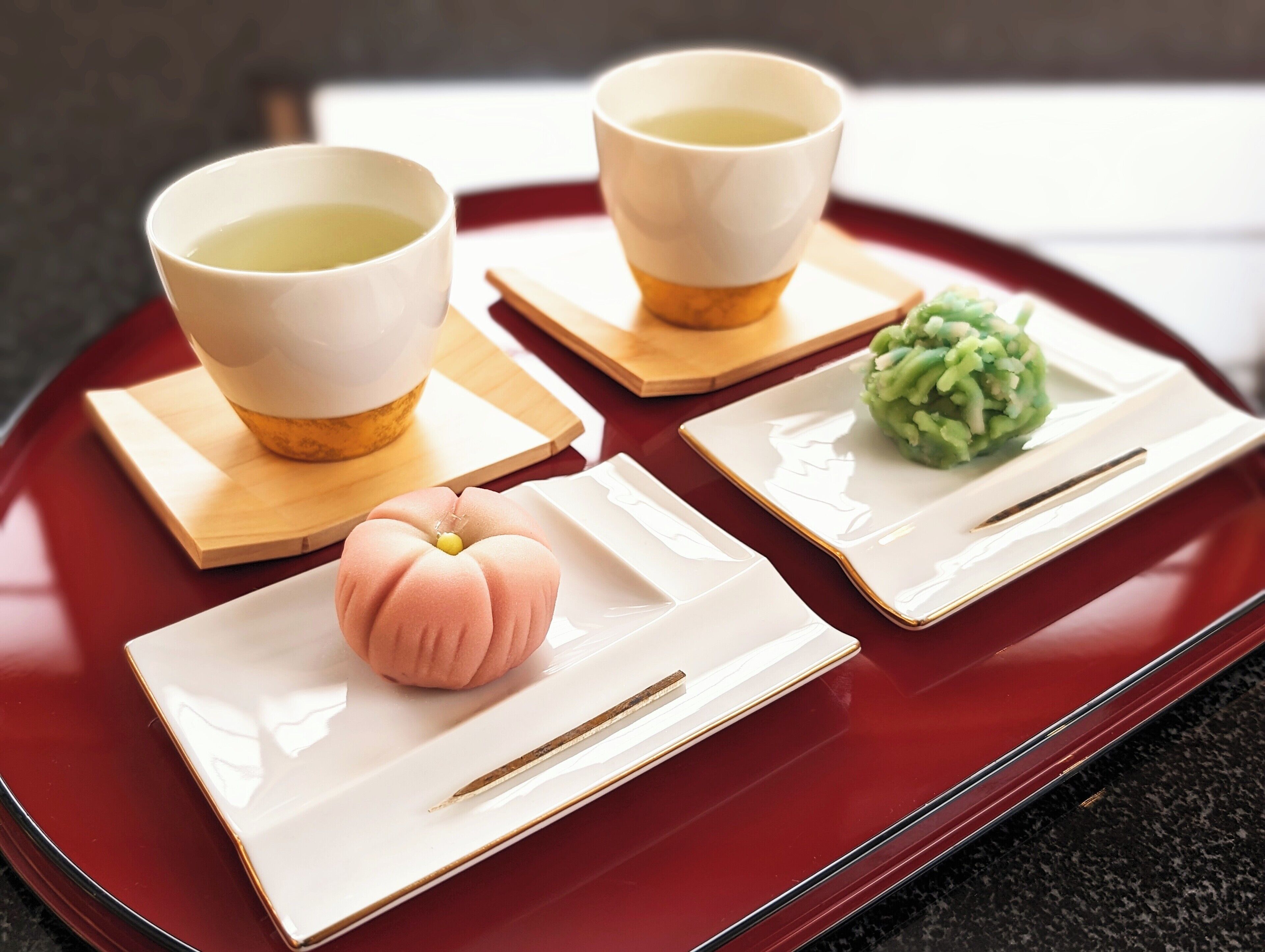 Una bandeja con dos tazas de té, un pequeño objeto rosa y un alimento verde en platos separados.