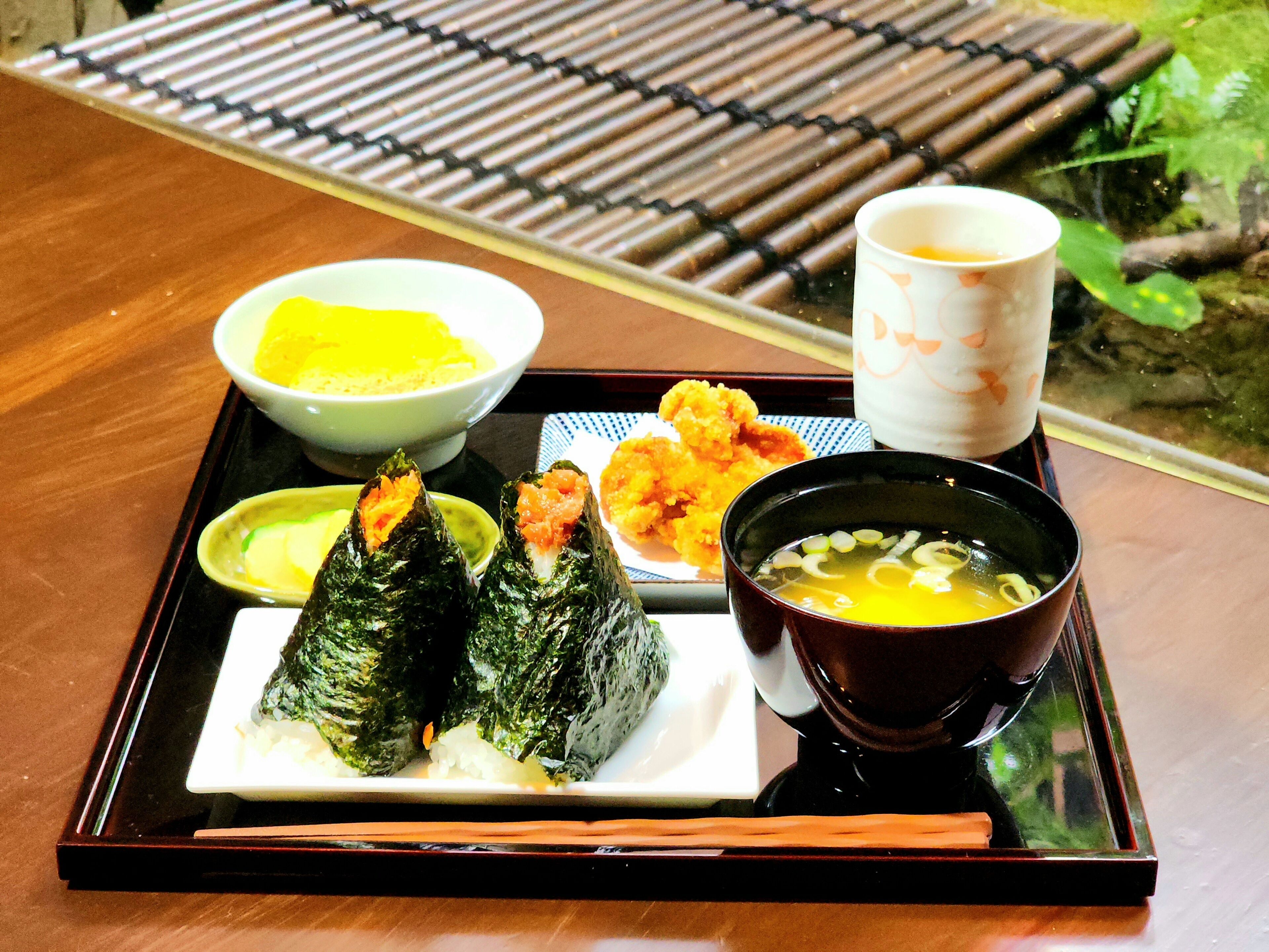 A tray with sushi, a bowl of soup, and a cup of tea on a wooden table.