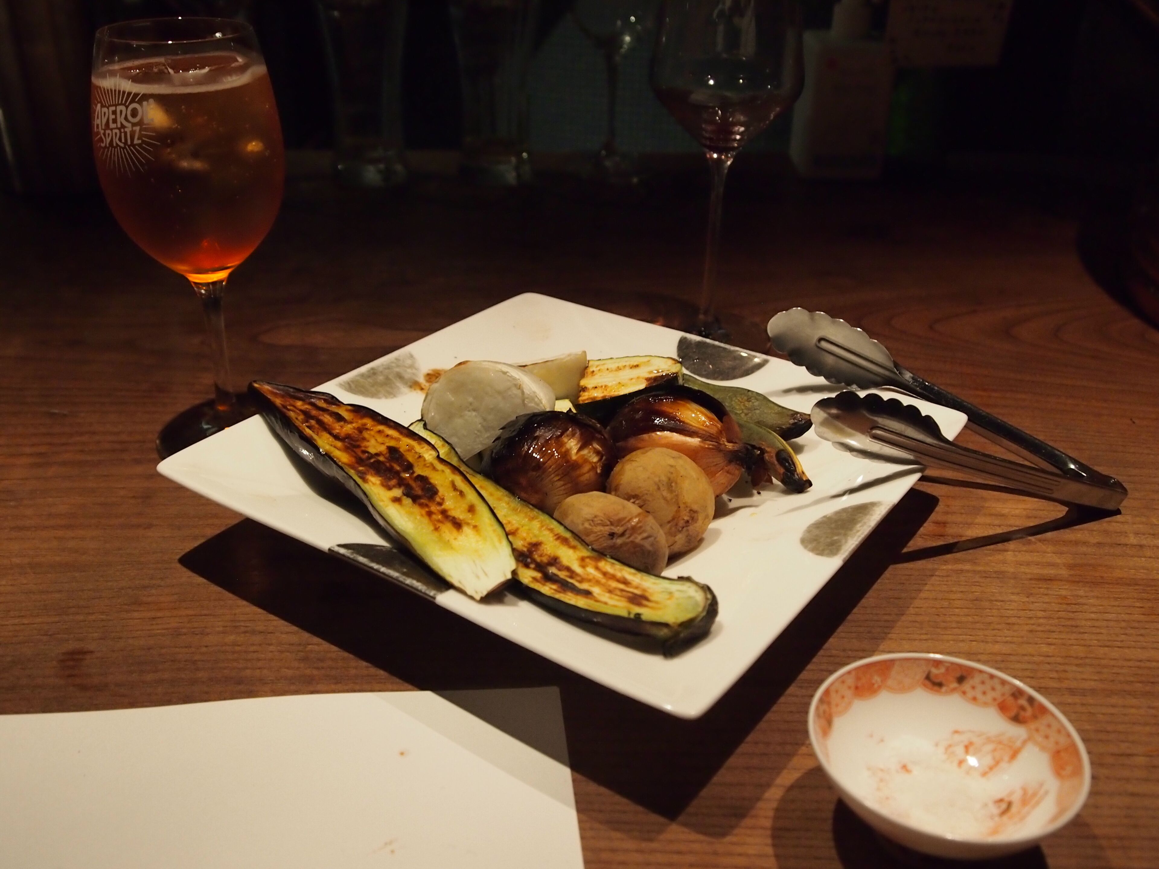 A plate of grilled vegetables and a glass of red wine on a wooden table.