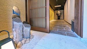 A hallway with a traditional Japanese-style entrance, featuring a wooden sliding door and a stone pathway leading to a room with a potted plant. - Rashiku Kanazawa (Kanazawa)