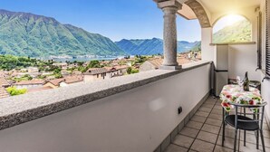 A balcony with a view of a mountainous landscape, a table with a tablecloth, and a bottle of wine.