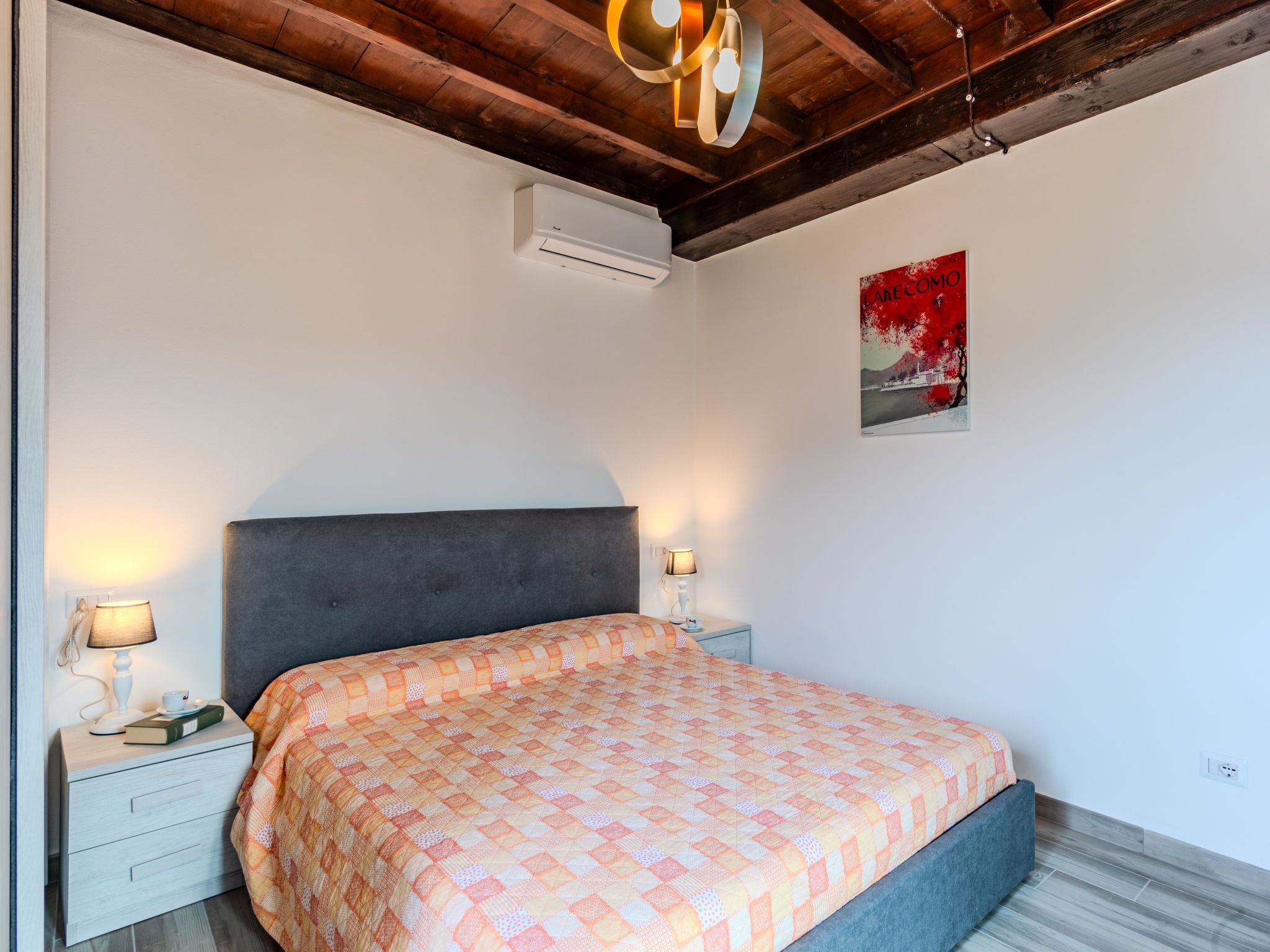 Un dormitorio con cama, dos mesitas de noche con lámparas, aire acondicionado y una obra de arte en la pared.