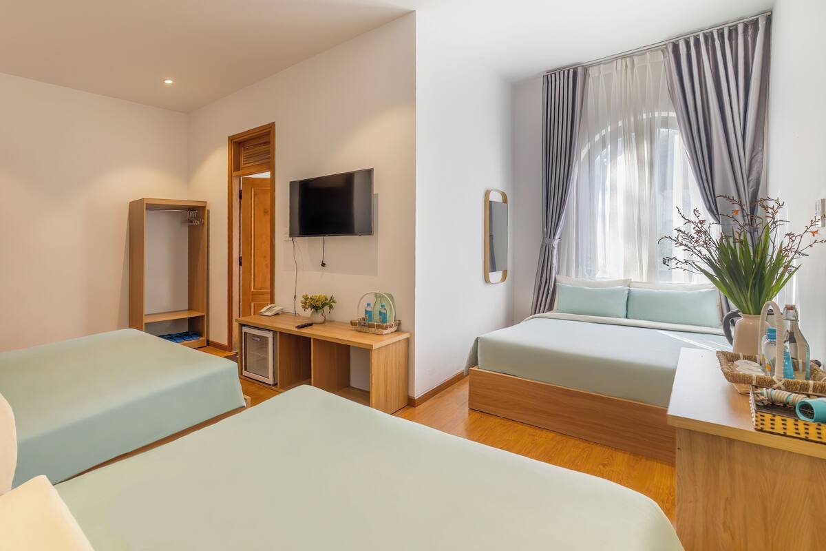 A hotel room with two beds, a desk with a TV, a mirror, and a window with curtains.