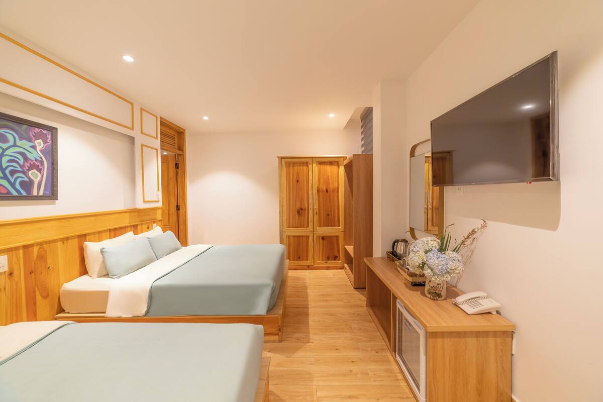 A hotel room with two beds, a wooden desk, a telephone, and a TV mounted on the wall.