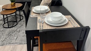 Ein moderner Essbereich mit einem schwarzen Esstisch, weißen Tellern und einem Glas Wasser. An den Wänden sind abstrakte Kunstwerke zu sehen, im Hintergrund ein schwarzes Sofa.