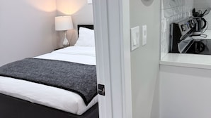 Ein modernes Hotelzimmer mit Bett, Nachttischlampe und einem kleinen Schreibtisch mit Kaffeemaschine.