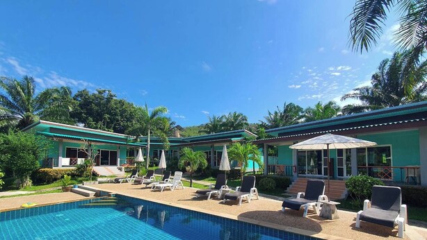 A swimming pool with lounge chairs and umbrellas, surrounded by greenery and a building with a green roof. - Tum Mai Kaew Lanta Resort (Ko Lanta)