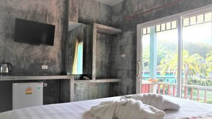 A hotel room with a bed, a small desk with a kettle, a refrigerator, a TV, and a balcony with a view of greenery. - Tum Mai Kaew Lanta Resort (Ko Lanta)