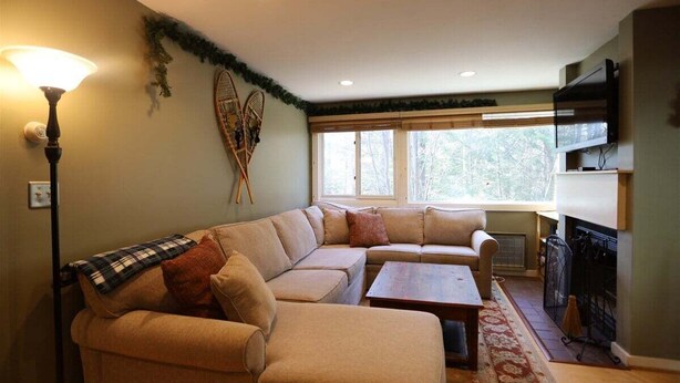 Ein Wohnzimmer mit Ecksofa, Couchtisch, Kamin und Fernseher.