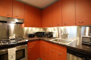 A kitchen with stainless steel appliances, orange cabinets, a sink, and a microwave.